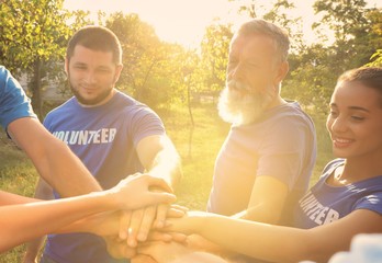 Group of volunteers joining hands together outdoors on sunny day