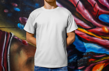 Wall Mural - Mockup white t-shirt on a young guy, against the background of a wall with graffiti, front view.