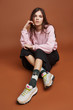 Full length shot of a dark-haired girl, sitting on a floor. She wearing pink sweatshirt, black culottes, black artwork socks with walking ladies with umbrella print and white sneakers. 