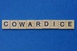 word cowardice made from brown wooden letters lies on a blue table 