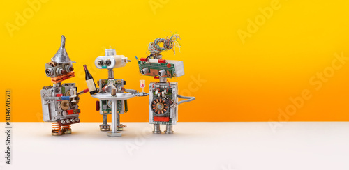 Robotic drink party. Three toy robots celebrate new system update. Yellow background, copy space