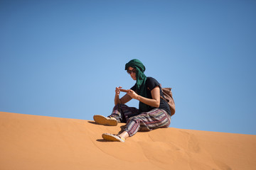 Girl looking at the mobile phone in the dunes of the Moroccan Sahara desert.