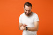 © ViDi Studio - Cheerful young man in casual white t-shirt posing isolated on bright orange wall background studio portrait. People sincere emotions lifestyle concept. Mock up copy space. Wearing smart watch on hand.