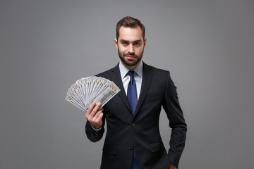 Wall Mural - Confident young business man in classic suit shirt tie posing isolated on grey background. Achievement career wealth business concept. Mock up copy space. Hold fan of cash money in dollar banknotes.