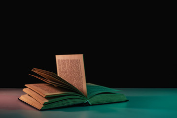 Fototapete - Beautiful open book in the color light on a table and night background.