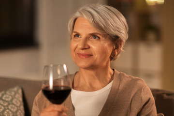 Canvas Print - people, alcohol and drinks concept - happy senior woman drinking red wine from glass at home in evening