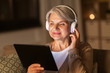 © Syda Productions - technology, people and lifestyle concept - happy senior woman in headphones and tablet pc computer listening to music at home in evening