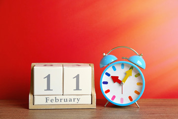 Canvas Print - Wooden block calendar and alarm clock on table against red background