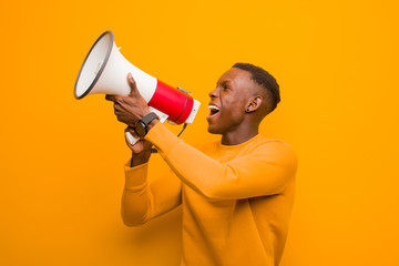 young african american black man against orange wall with a megaphone