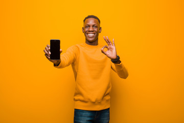 young african american black man against orange wall with a smart phone