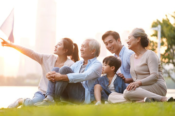 Wall Mural - three generation happy asian family sitting on grass enjoying good time at dusk outdoors in park