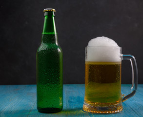 Mug of beer and green bottle with beer on wooden table on dark background