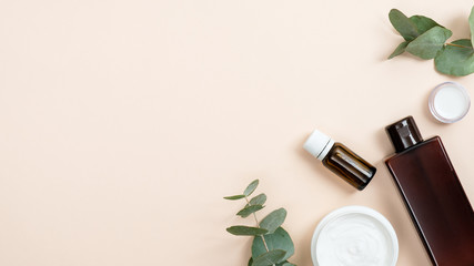 Wall Mural - Organic cosmetic products in glass bottle containers and cream jar with eucalyptus leaves on pastel beige background. Bio organic product, zero waste cosmetic concept