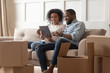 © fizkes - African couple sit on couch near boxes using tablet computer