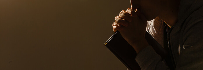 Poster - Religious young man praying to God on dark background, black and white effect