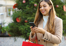 Christmas Woman Buying Online On The Smart Phone In The Street With Christmas Tree On Background.