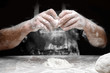 Baker chef sprinkling flour fresh dough on kitchen table, black background