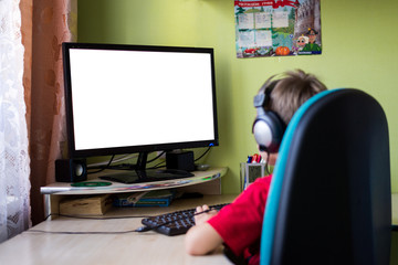 child at the table wearing headphones at the computer white screen for text