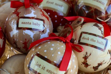 Different colorful toys for traditional Christmas tree such as balls with New year inscriptions and red ribbons lying in a wicker basket. Winter holidays background. Close up.