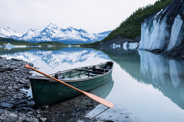 canoe resting on rock covered ice of valdez glacier with icebergs behind. valdez, alaska.