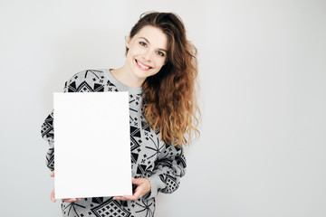 Happy european girl holding a blank vertical canvas in her hands. Empty frame for text or photo. Young woman with mockup poster on grey background.