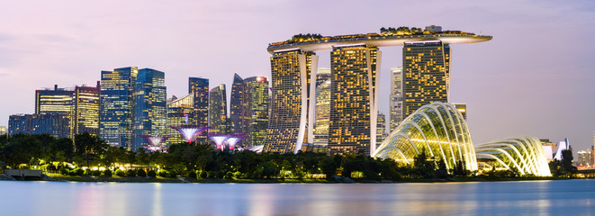 Stunning panoramic view of the illuminated skyline of Singapore during a dramatic sunset in the background and a calm bay in the foreground. Singapore is an island city-state of southern Malaysia.