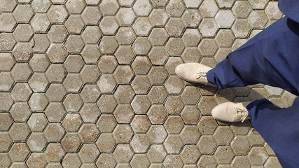 Wet paving stones with two legs in grey shoes.