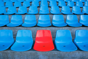 Single or one red seat or bench in the middle or center of blue chair in the football or soccer stadium.