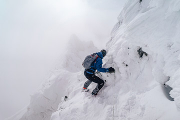 Wall Mural - An alpinist climbing an alpine ridge in winter extreme conditions. Adventure ascent of alpine peak in snow and on rocks. Climber ascent to the summit. Winter ice and snow climbing in mountains.