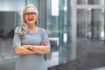 Wall Mural - Older business woman CEO standing and smiling confident, successful, at office building with copy space