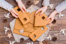 Parts Of A Disassembled Christmas Gingerbread House In Children's Hands And Christmas Decorations On A Wooden Background. Top View. Christmas Preparations