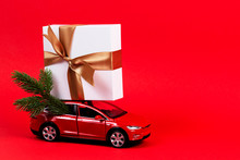 Christmas Background. Red Toy Car With Christmas Tree Fir Branch And Present Gift Box On Red Background