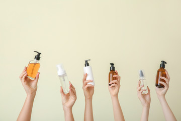 Female hands with different cosmetic products in bottles on color background