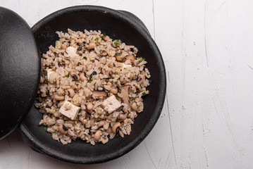 Baião de Dois - Brazilian Traditional Food - made with sausage, curd cheese, dried beef and rice in a black clay pot, on white background. Typical dish of Northeast Brazil.