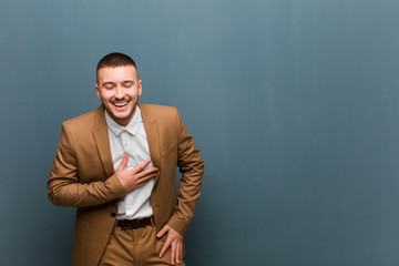 young handsome businessman laughing out loud at some hilarious joke, feeling happy and cheerful, having fun against flat background