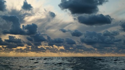 Wall Mural - Ripples on surface of sea on background of sky with clouds at sunset.