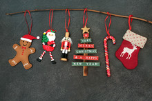 Christmas Decorations Hanging On A Branch With Nutcracker Soldier, Tree, Candy Cane, Stocking And Gingerbread Man On Grey Grunge Background With Copy Space.