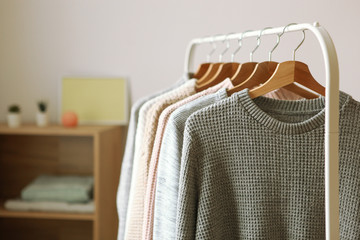 Wall Mural - Warm sweaters on a wardrobe hanger on a light background. Autumn, winter clothes.