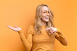 © kues1 - young pretty blonde woman smiling cheerfully and pointing to copy space on palm on the side, showing or advertising an object against flat color wall