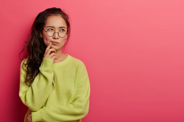 Wall Mural - Contemplative female looks seriously and pensively aside, purses lips and concentrated above, dressed in green loose jumper, makes choice in mind, remembers information, ponders on something