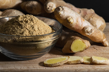 Ginger powder in glass bowl on wooden cutting board with ginger roots and slices. Healthy eating concept.