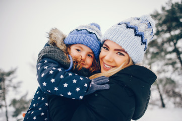 Family have fun in a winter park. Stylish mother in a black jacket. Little girl in a blue hat