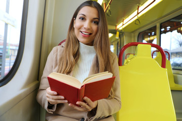 Canvas Print - Beautiful young woman sitting in tram caught and surprised at reading her book looks at camera.