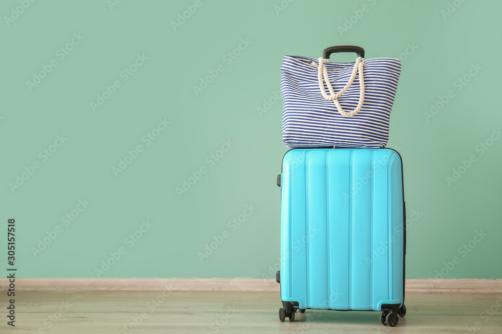 Suitcase and beach bag near color wall. Travel concept