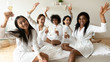 © fizkes - Happy diverse young women raise champagne glasses look at camera