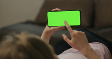 Young Woman Lying On A Couch And Using Smartphone With Horizontal Green Screen