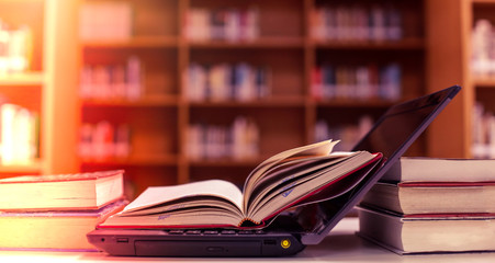 Poster - stack of books with laptop on table in library.