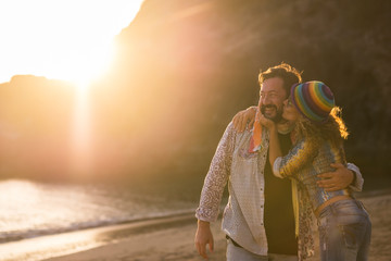 Love concept with happy adult caucasian couple kissing and hugging with joy in outdoor leisure activity at the beach during summer holiday vacation - coloured beautiful sunset in backgorund