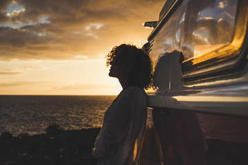 Travel and independence concept with woman in silouette and old vintage camper van - coloured dawn sunset in background with ocean and horizon