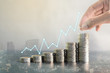 © mzsorasak - Double exposure hand stacking coins on blur background of city with profit line chart growth up. Business, finance, marketing, e-commerce concept and design